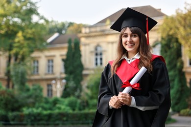 Happy student with diploma after graduation ceremony outdoors, space for text