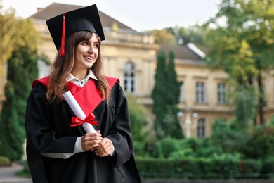 Photo of Happy student with diploma after graduation ceremony outdoors, space for text