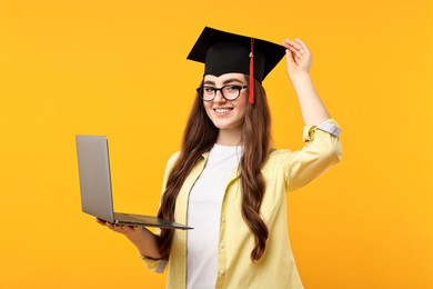 Photo of Happy student with laptop after graduation on orange background