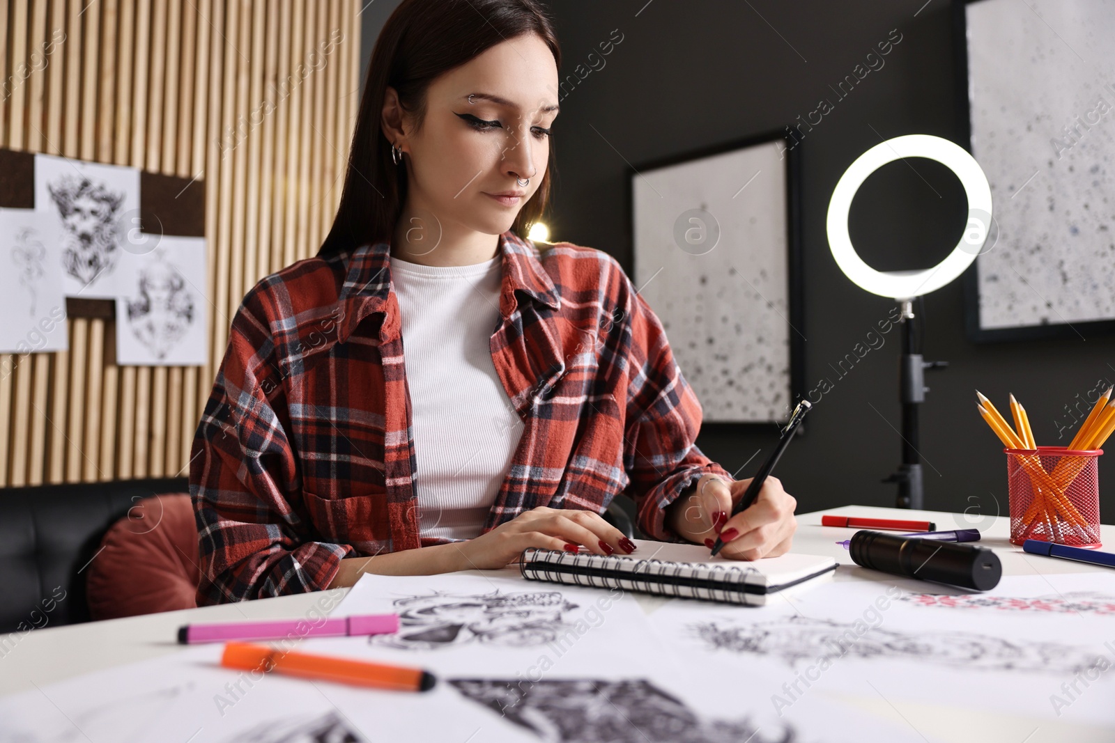 Photo of Tattoo artist drawing sketch with pen at white table in salon