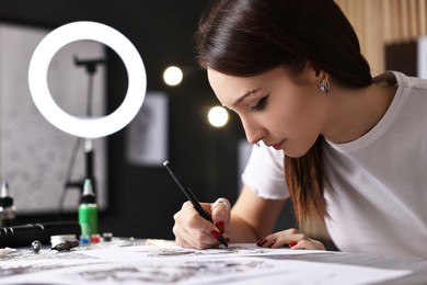 Photo of Tattoo artist drawing sketch at table with supplies in salon