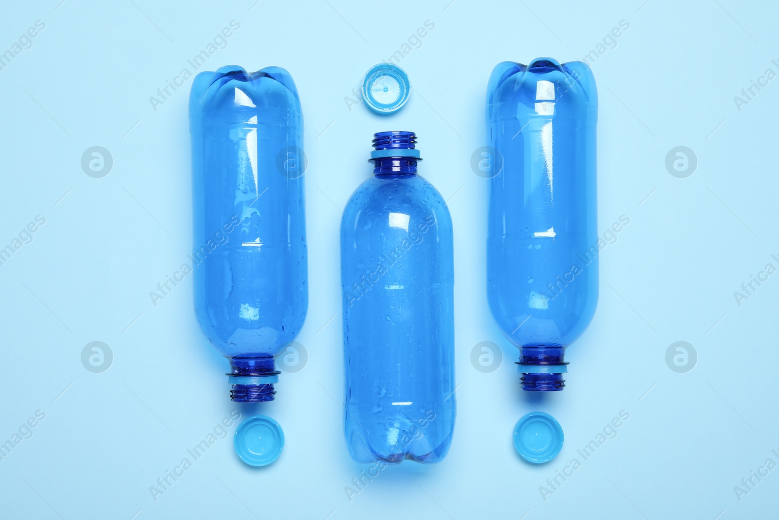 Photo of Plastic bottles and caps on light background, top view