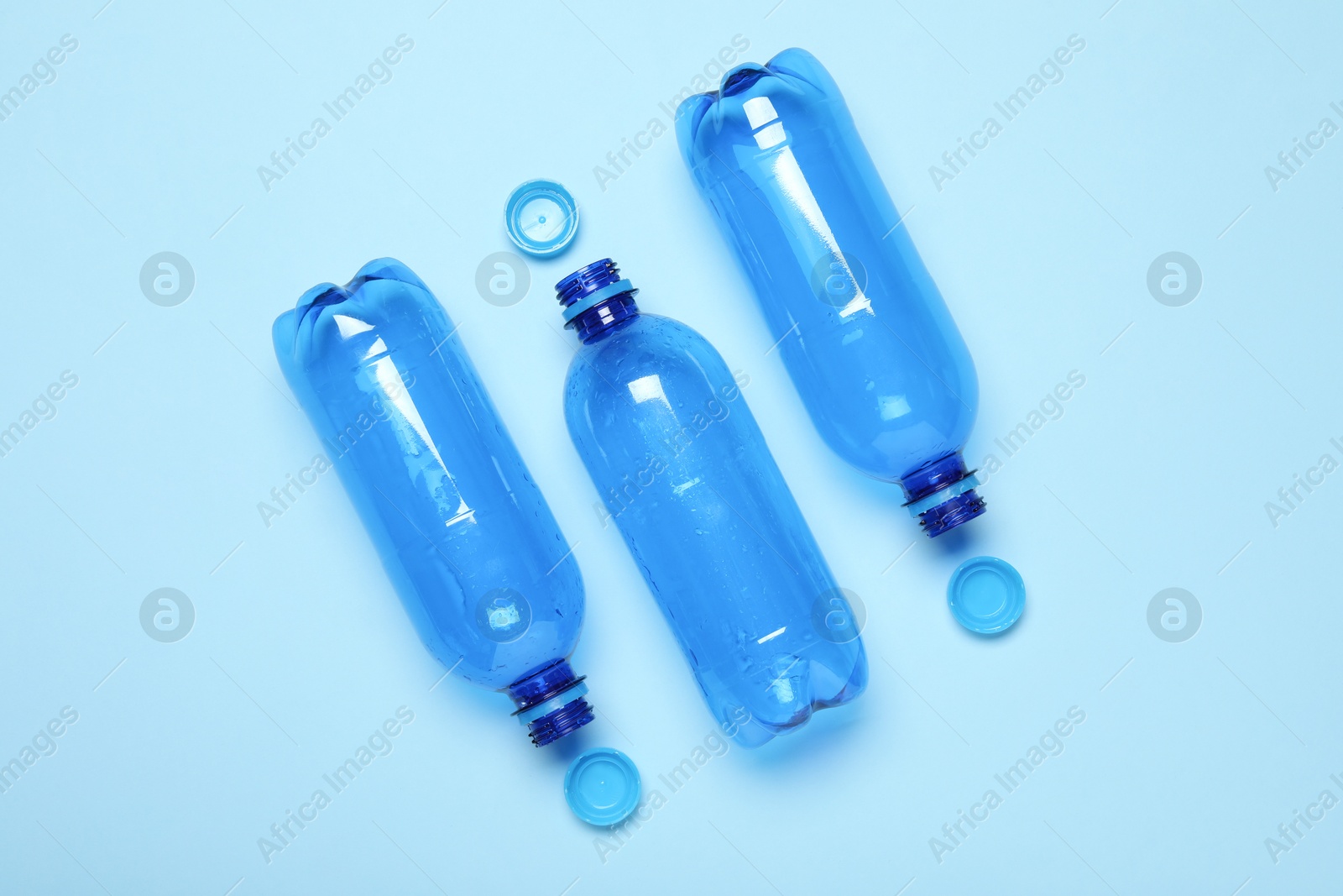 Photo of Plastic bottles and caps on light background, top view