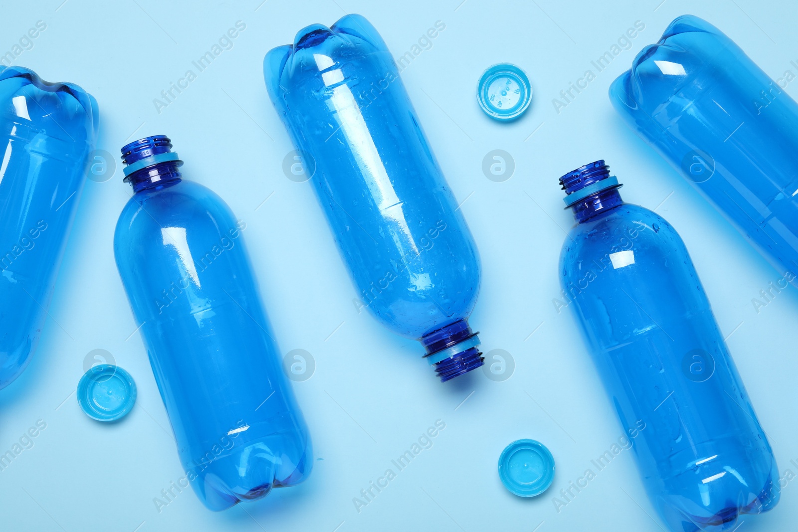 Photo of Plastic bottles and caps on light background, top view