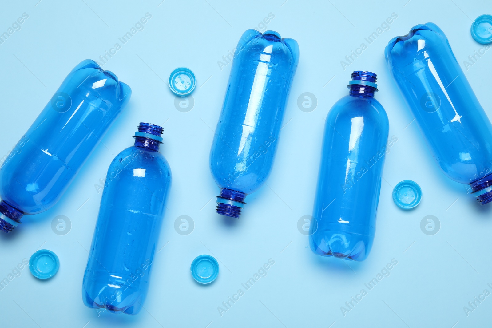 Photo of Plastic bottles and caps on light background, top view