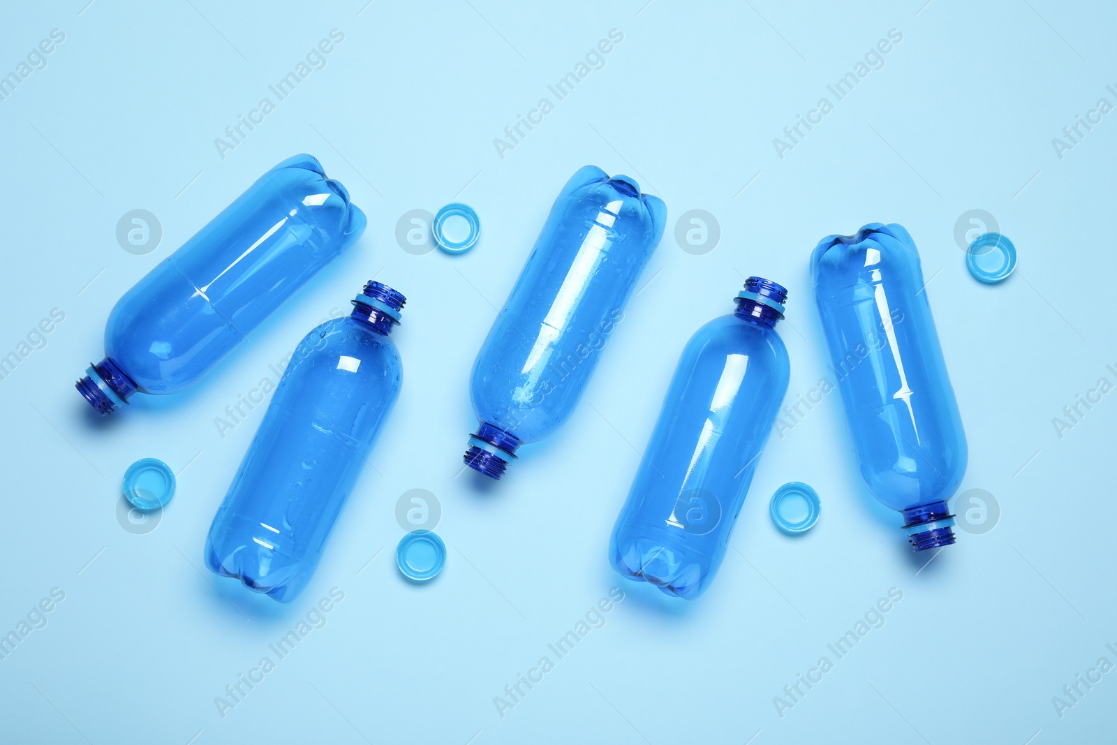 Photo of Plastic bottles and caps on light background, top view