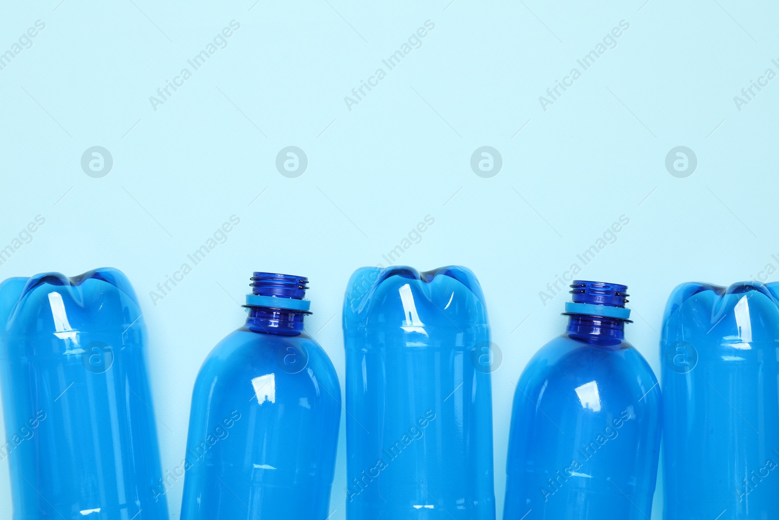 Photo of Empty plastic bottles on light blue background, flat lay. Space for text