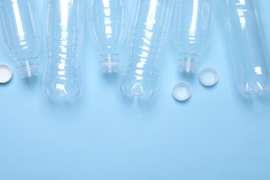 Empty plastic bottles on light blue background, flat lay. Space for text