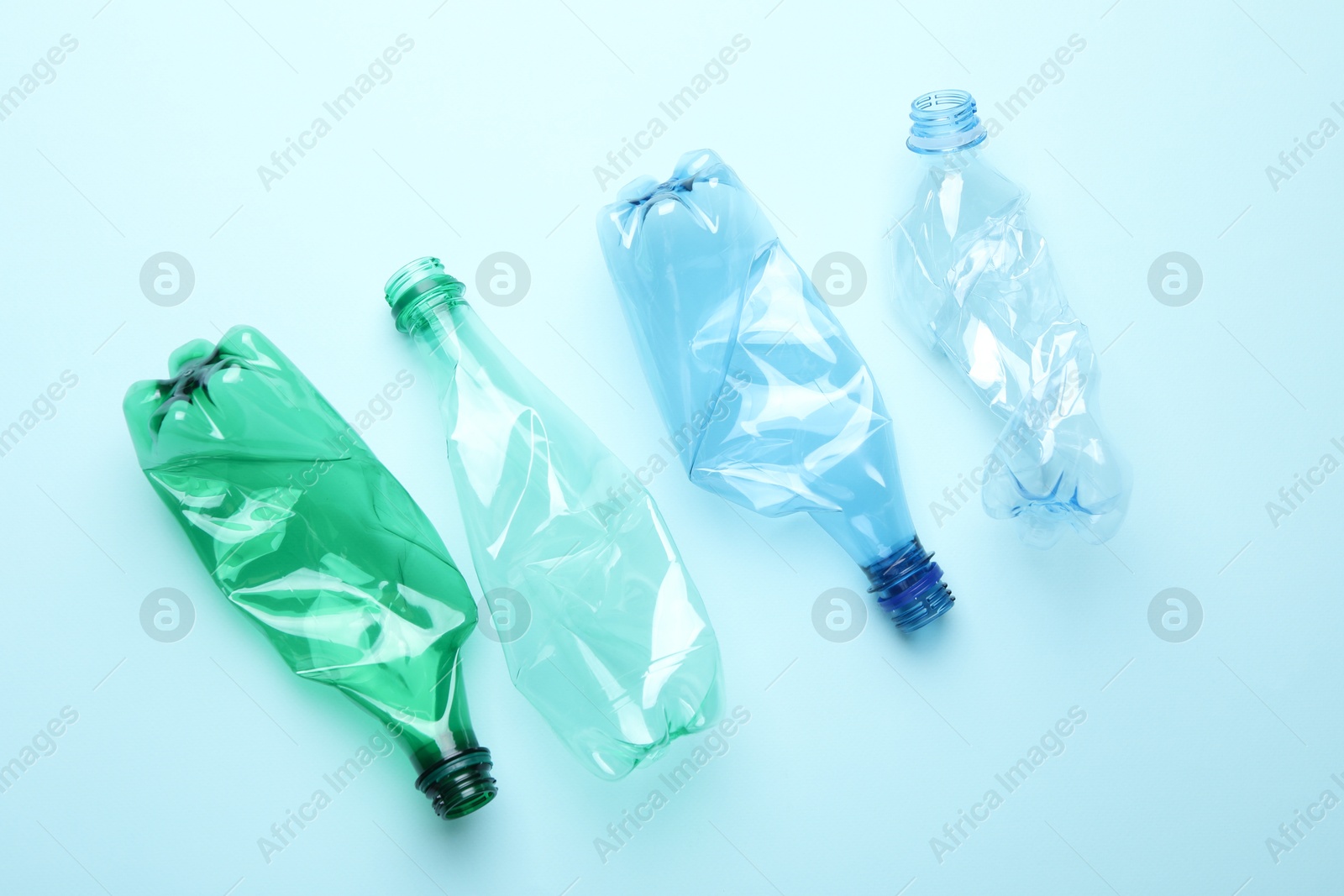 Photo of Crumpled plastic bottles on light blue background, flat lay