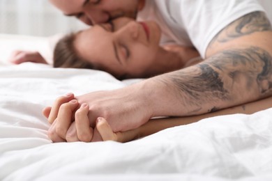 Man kissing his girlfriend in bed, focus on hands