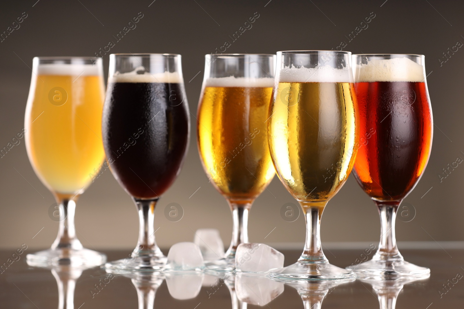 Photo of Glasses with different types of beer and ice cubes on mirror surface, closeup