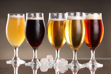 Photo of Glasses with different types of beer and ice cubes on mirror surface, closeup