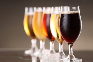 Photo of Glasses with different types of beer and ice cubes on mirror surface, closeup