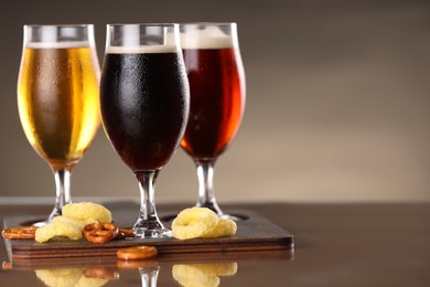 Photo of Glasses with different types of beer and snacks on mirror surface. Space for text