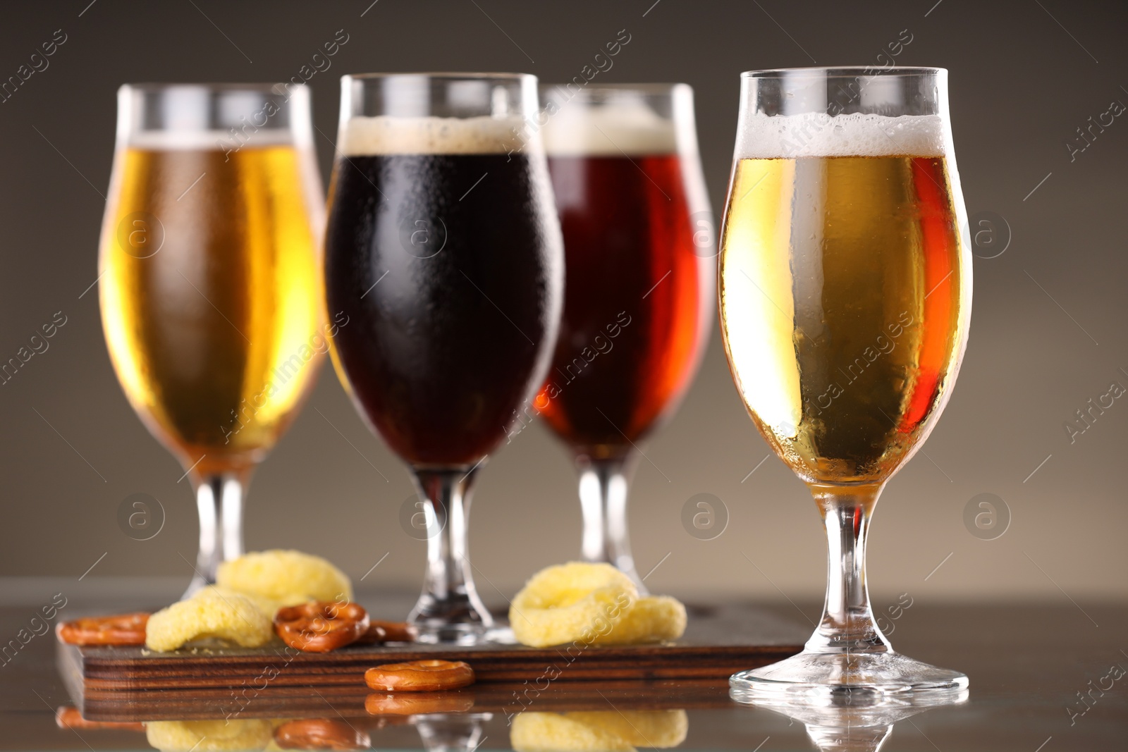 Photo of Glasses with different types of beer and snacks on mirror surface, closeup