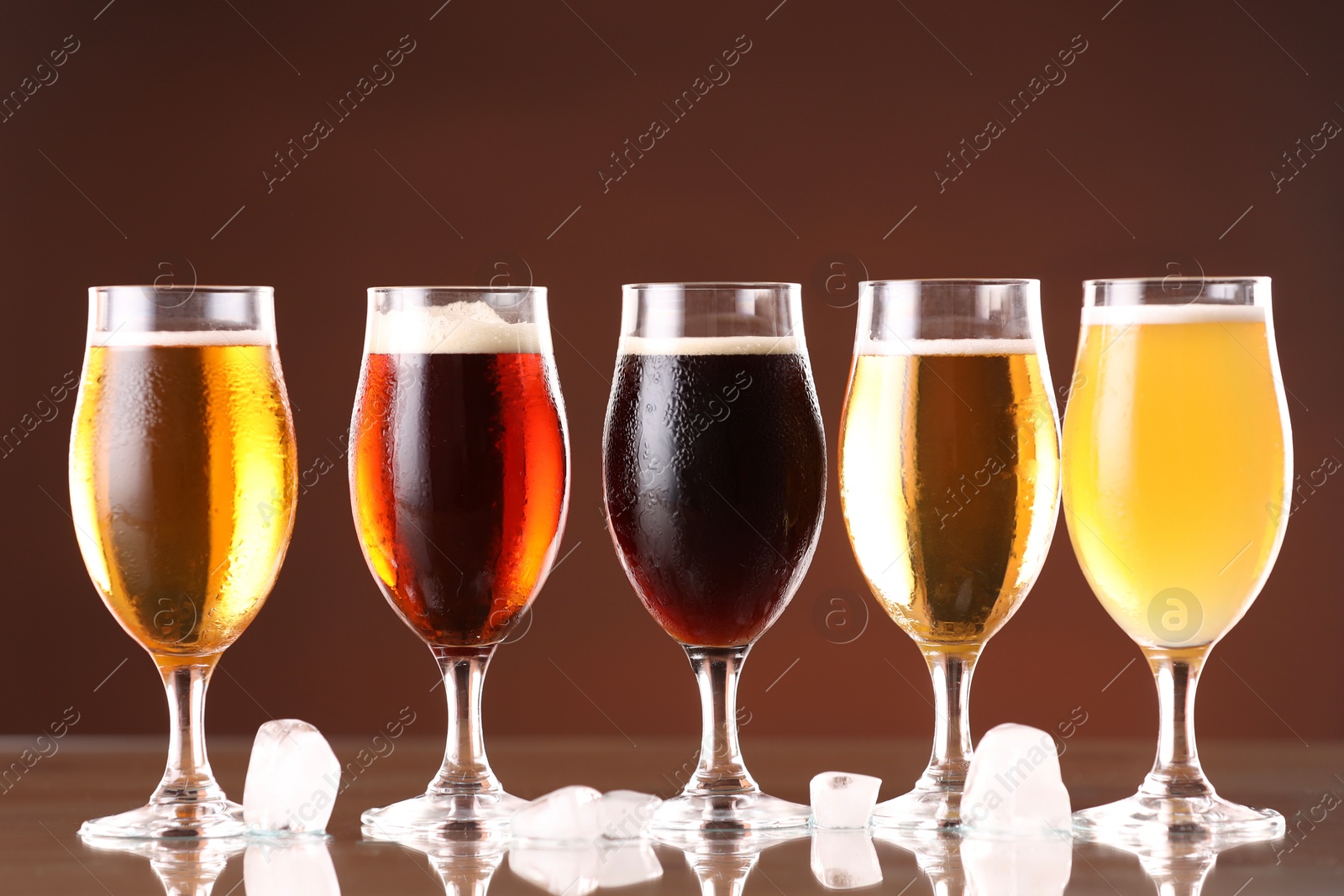 Photo of Glasses with different types of beer and ice cubes on mirror surface