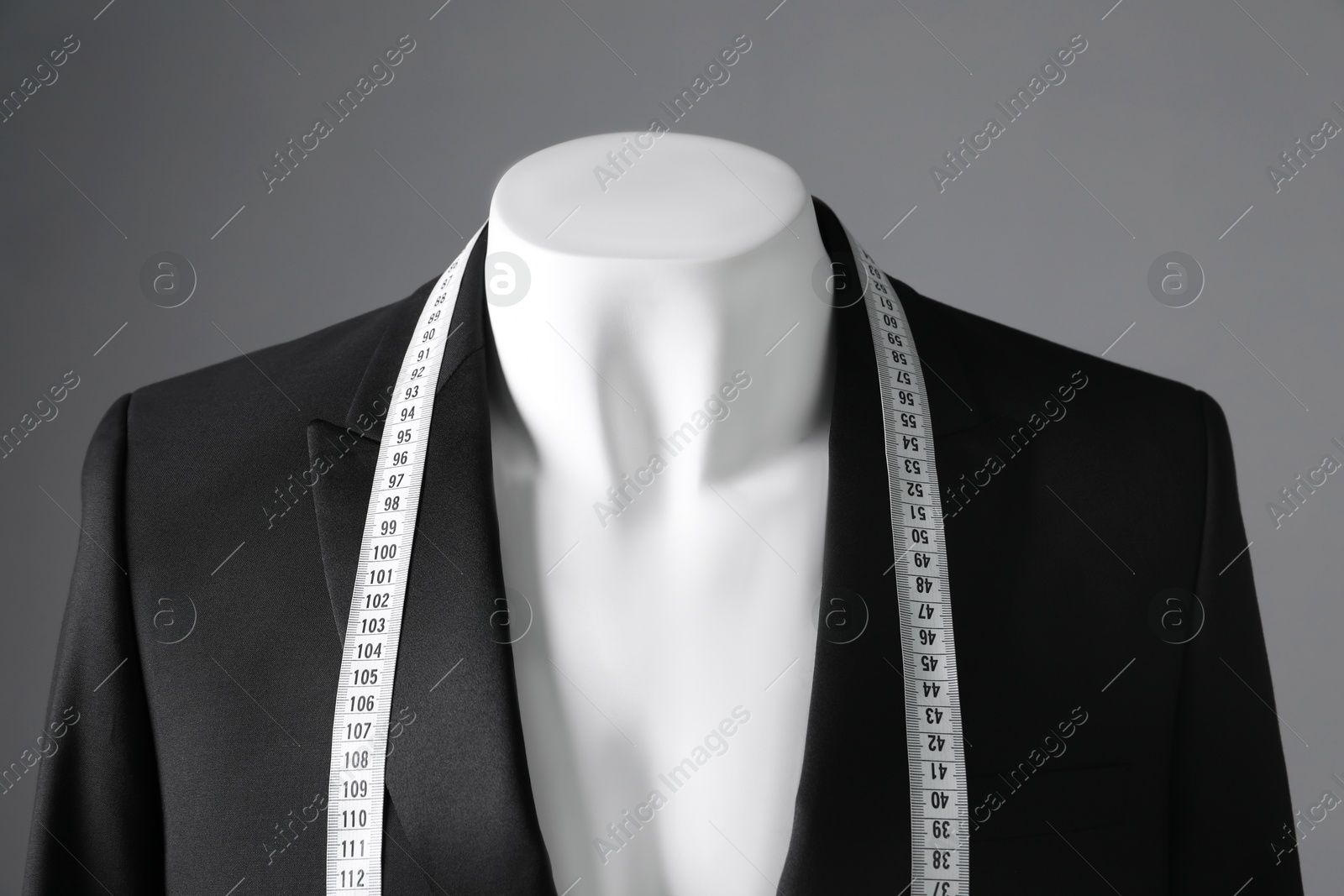 Photo of Male mannequin with black jacket and measuring tape on grey background, closeup