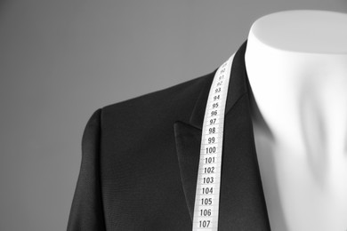 Photo of Mannequin with black jacket and measuring tape on grey background, closeup