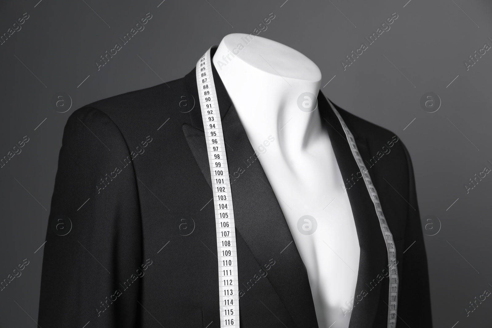 Photo of Male mannequin with black jacket and measuring tape on grey background, closeup