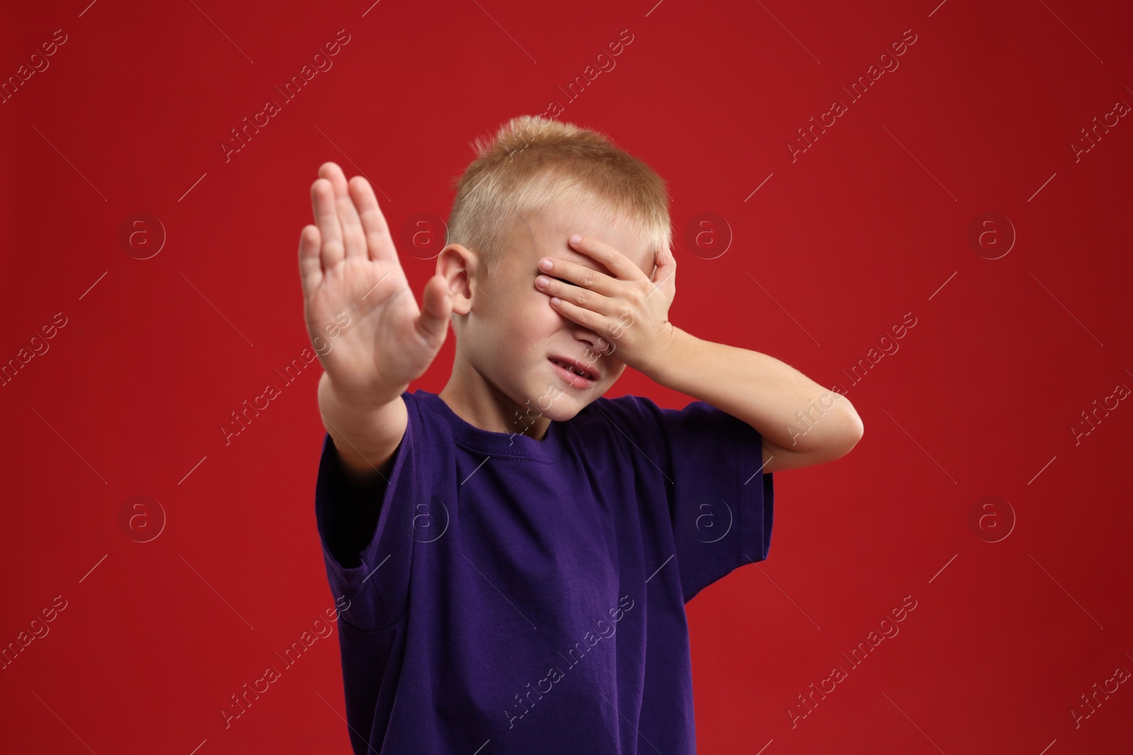 Photo of Scared little boy covering eyes on red background