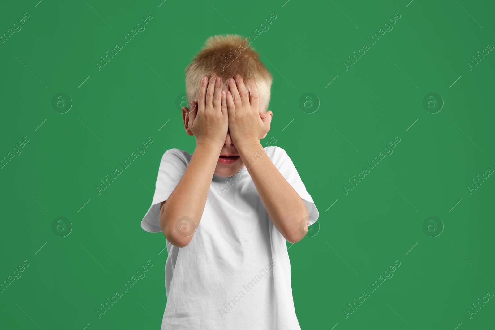 Photo of Scared little boy covering face with hands on green background