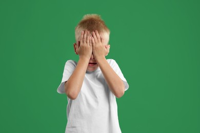 Scared little boy covering face with hands on green background