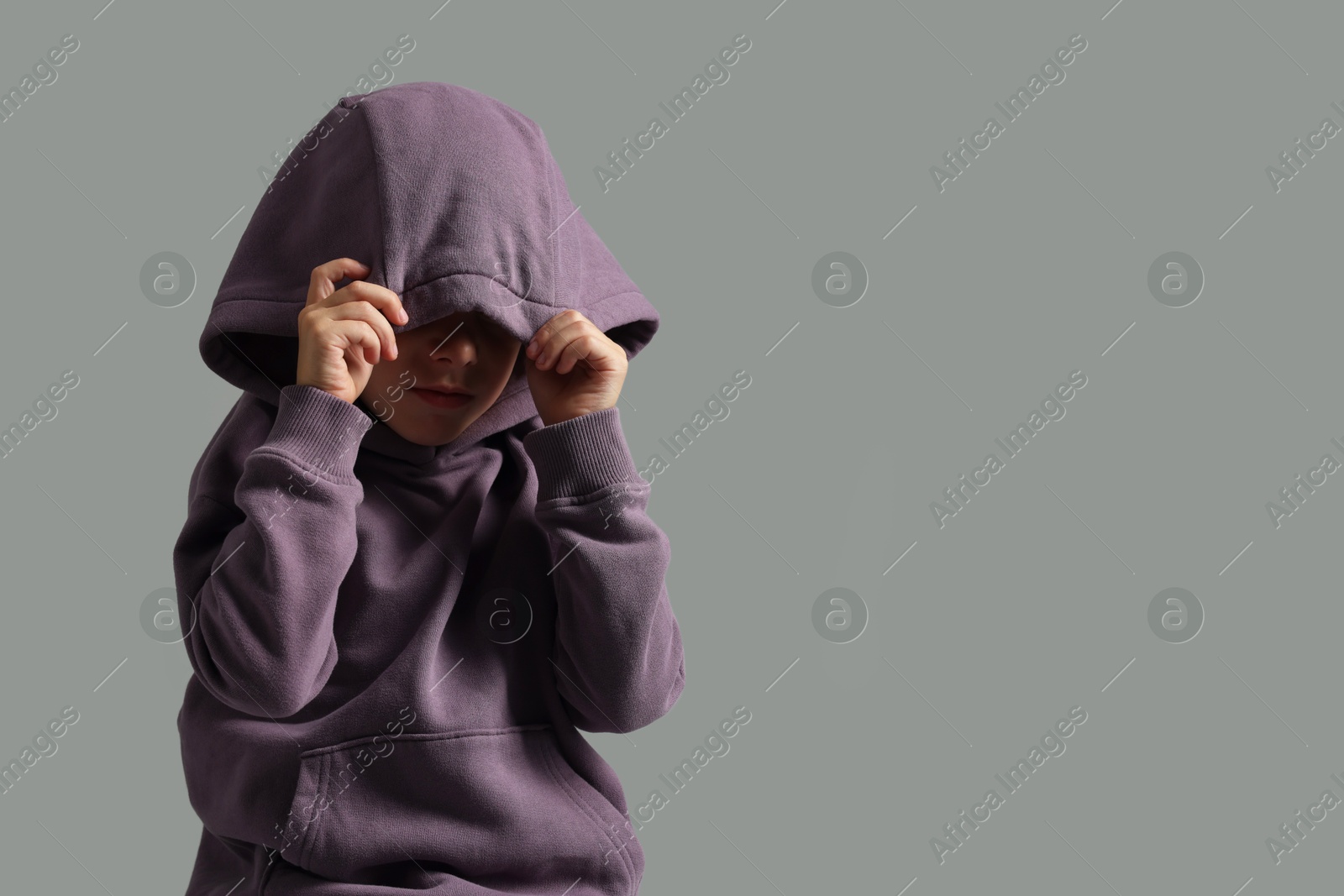 Photo of Scared little boy hiding on grey background. Space for text