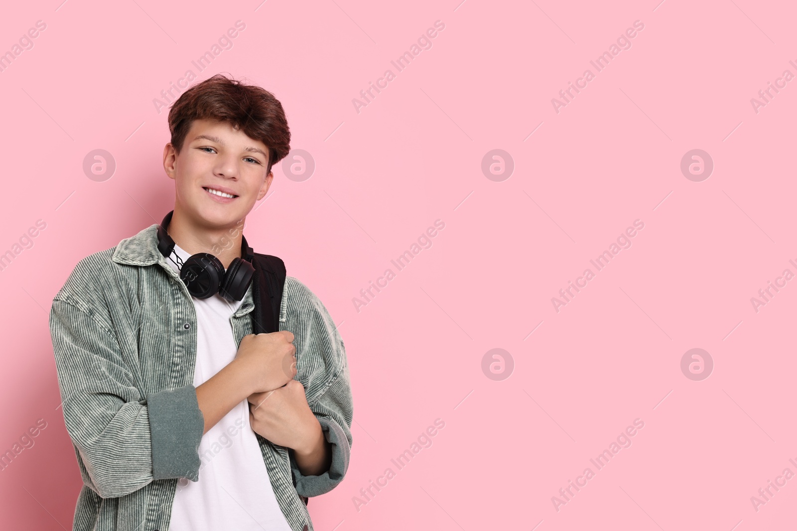 Photo of Happy teenage boy with headphones and backpack on pink background, space for text