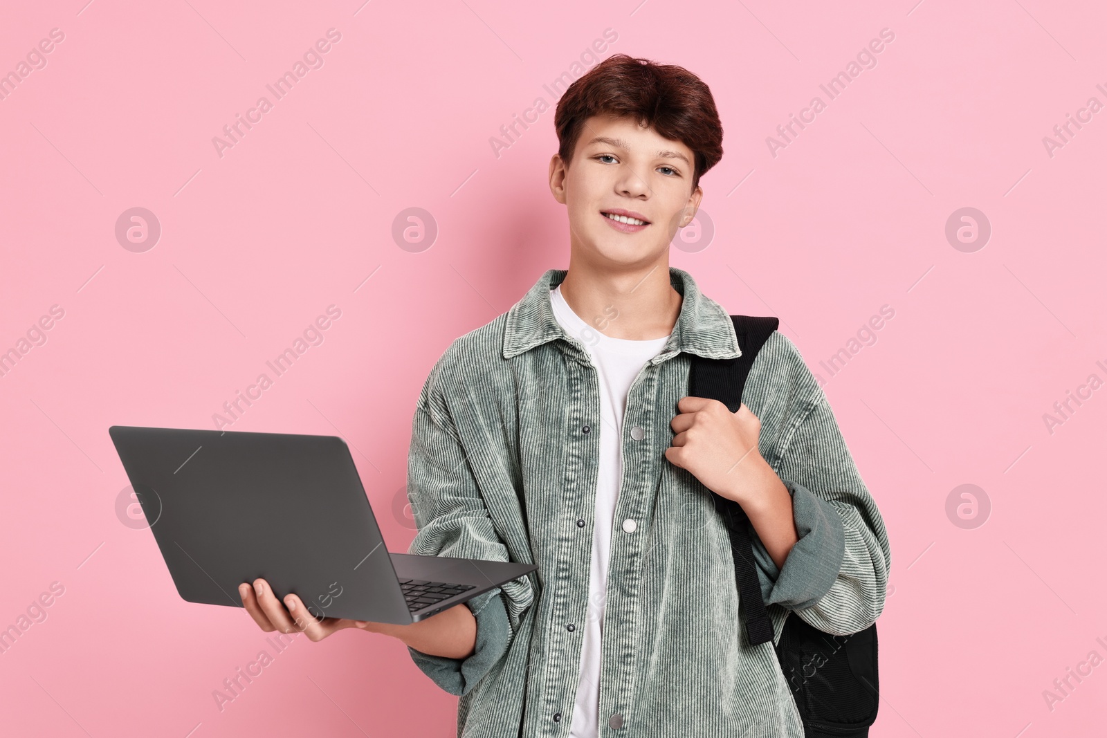 Photo of Happy teenage boy with laptop and backpack on pink background