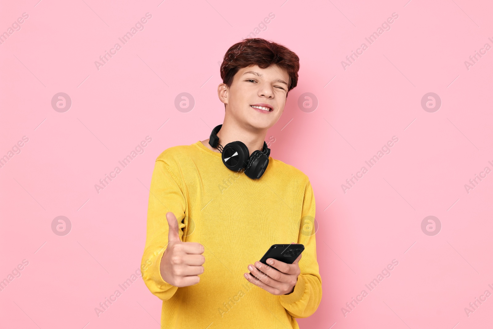 Photo of Teenage boy with headphones and smartphone showing thumbs up on pink background