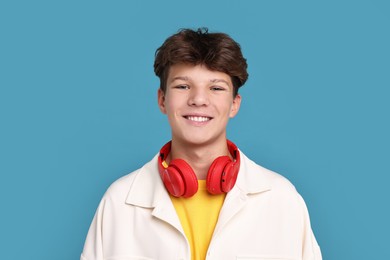 Happy teenage boy with headphones on light blue background