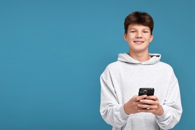 Teenage boy with smartphone on light blue background, space for text