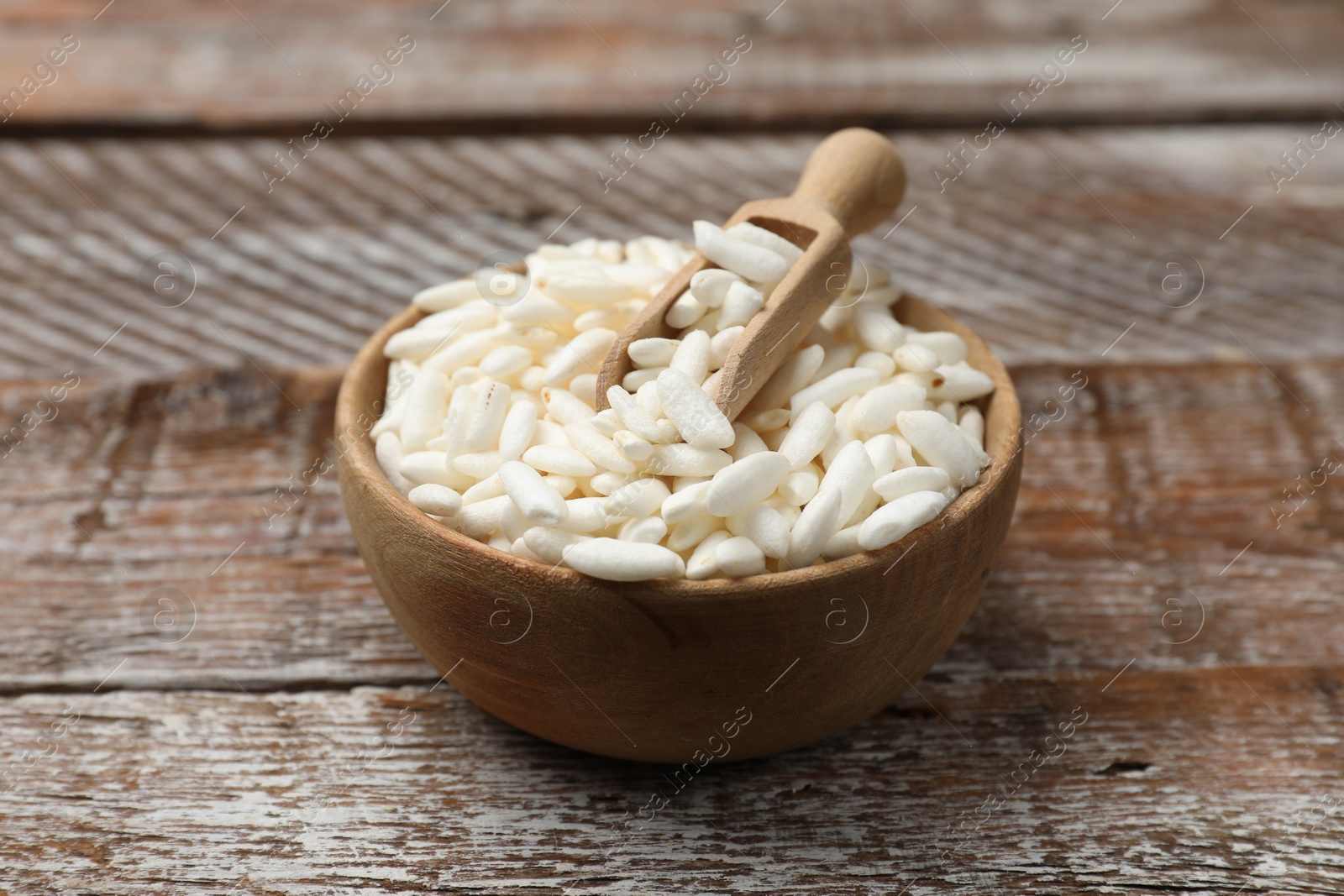 Photo of Puffed rice in bowl and scoop on wooden table, closeup