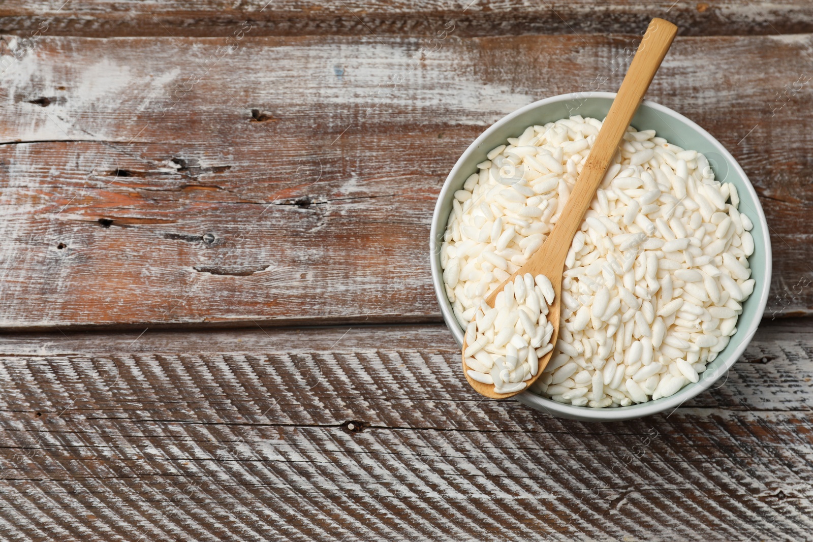 Photo of Puffed rice in bowl and spoon on wooden table, top view. Space for text