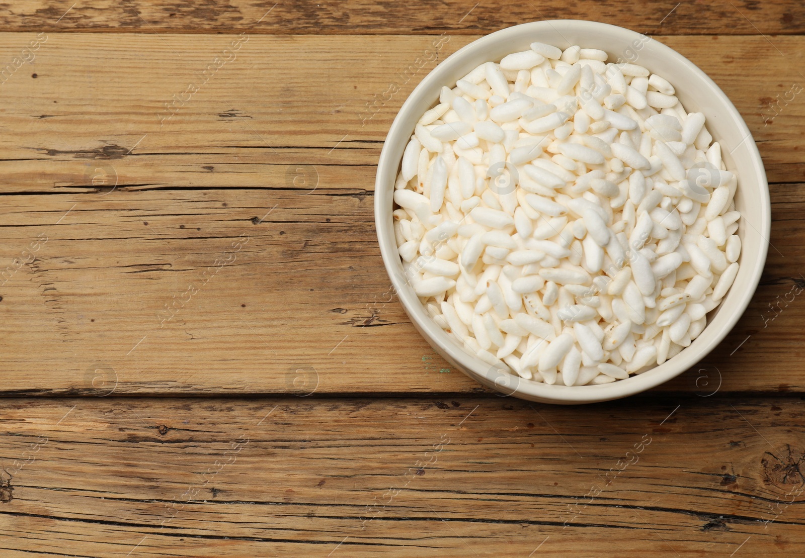 Photo of Puffed rice in bowl on wooden table, top view. Space for text