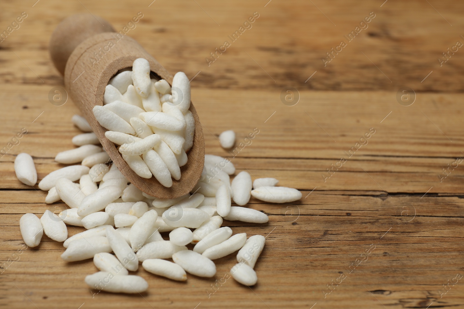 Photo of Puffed rice in scoop on wooden table, closeup. Space for text