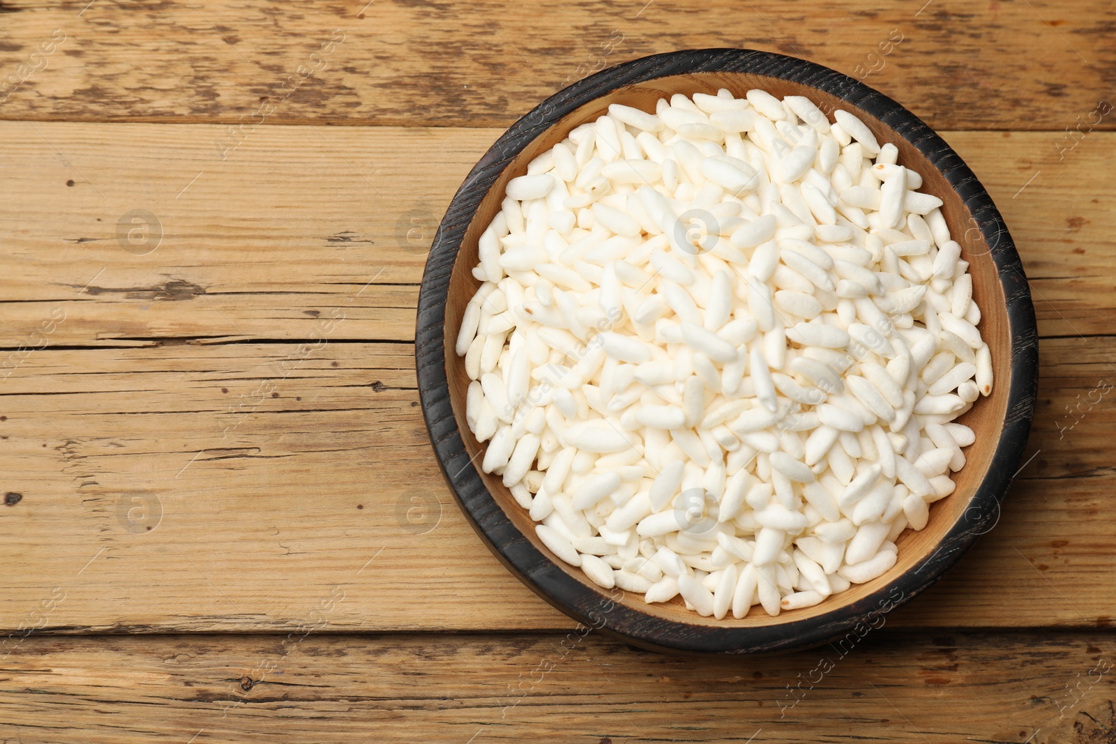 Photo of Puffed rice in bowl on wooden table, top view. Space for text