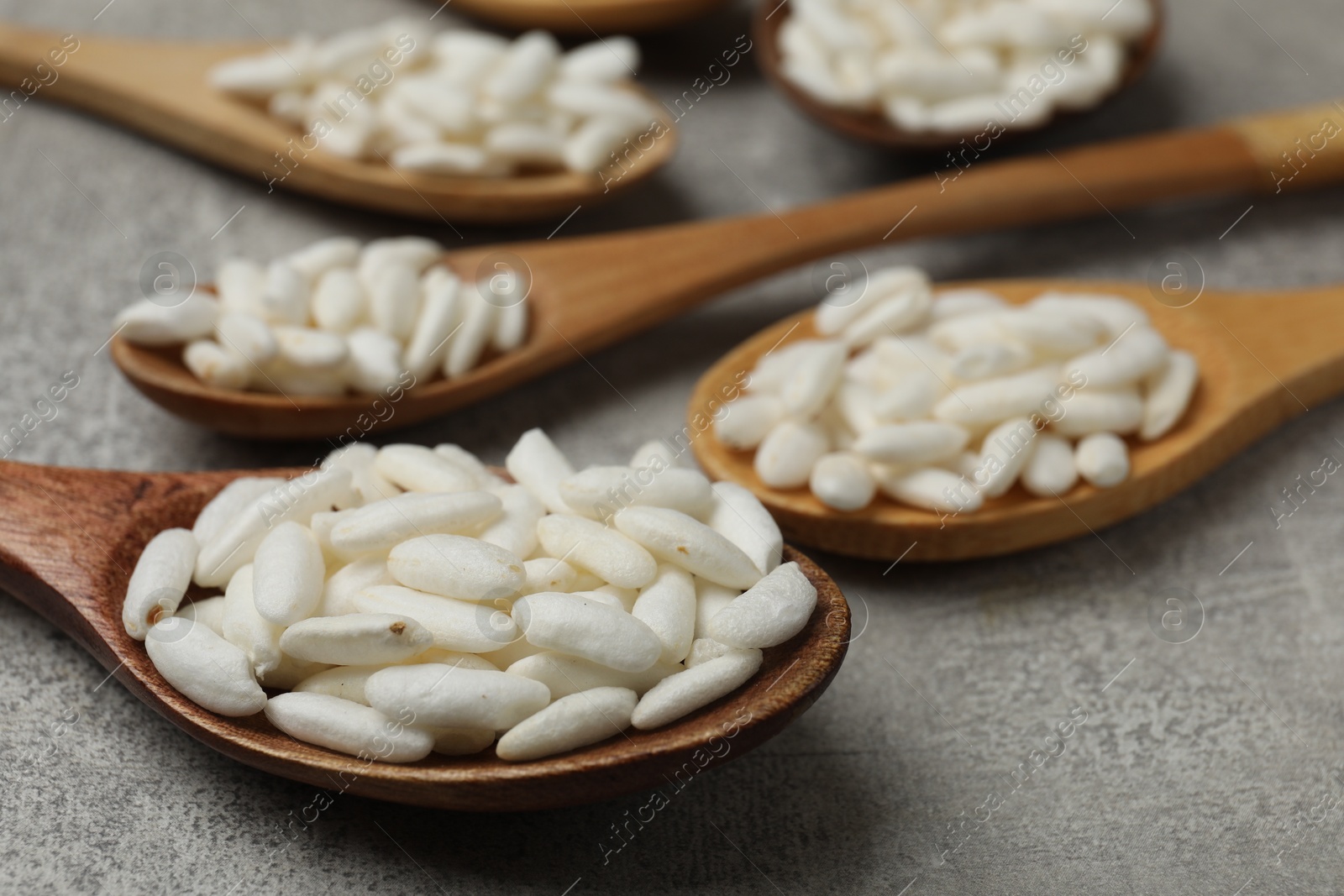 Photo of Puffed rice in wooden spoons on light grey table, closeup