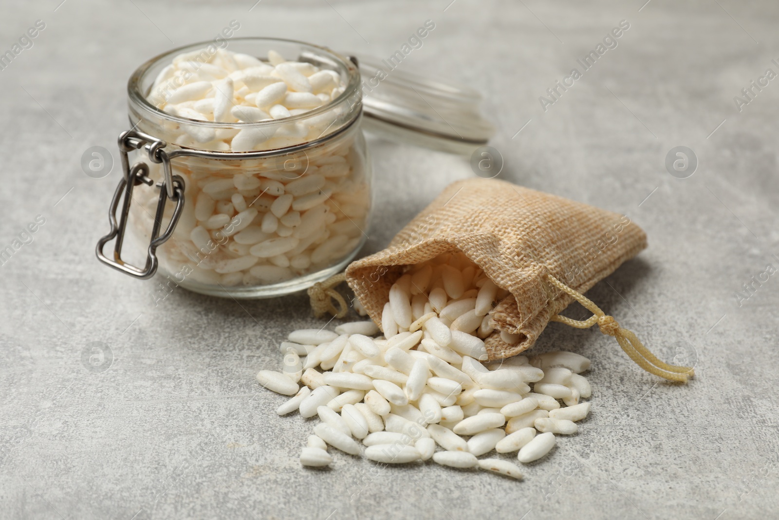 Photo of Puffed rice in jar and sack on light grey table, closeup