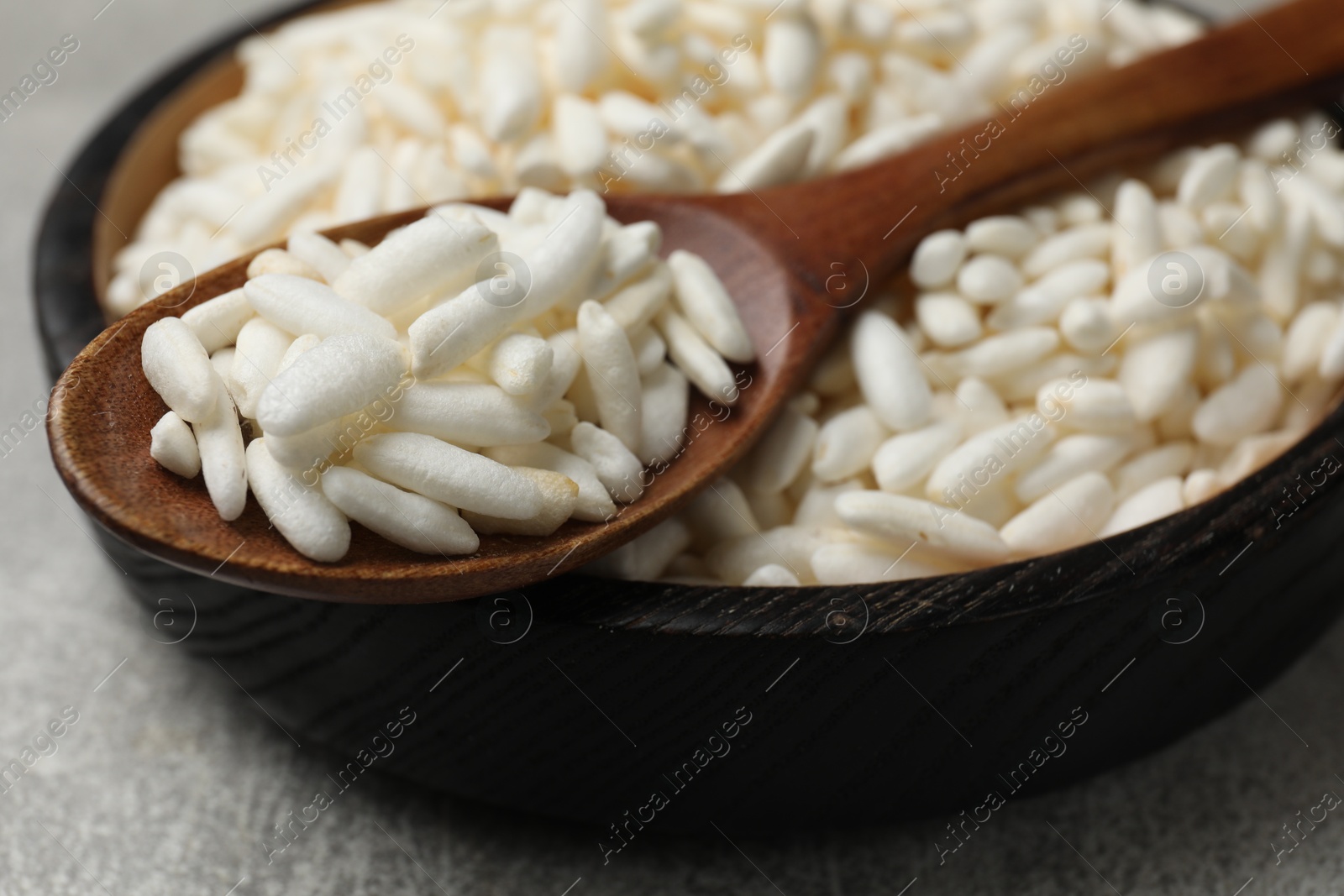 Photo of Puffed rice in bowl and spoon on light grey table, closeup