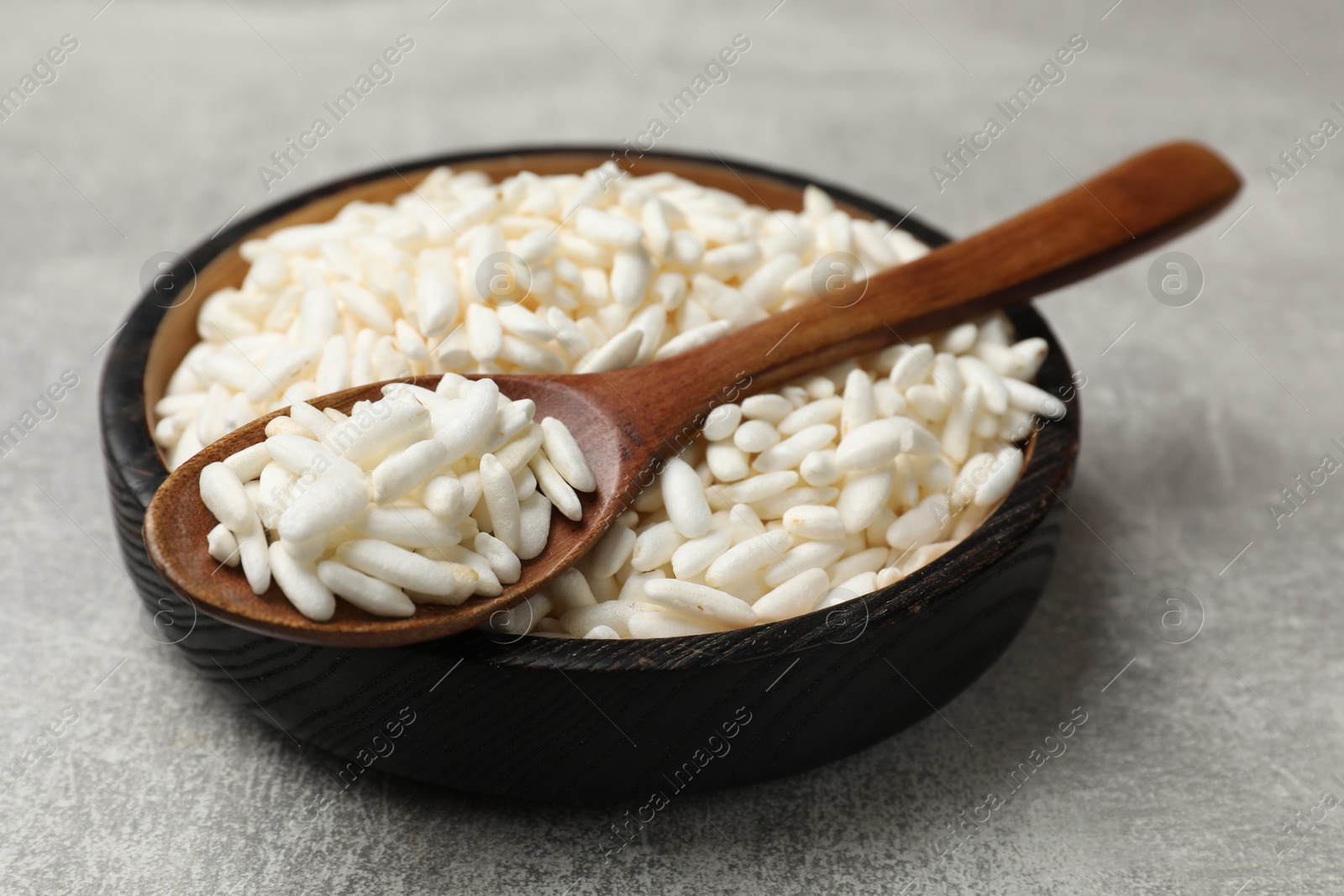 Photo of Puffed rice in bowl and spoon on light grey table, closeup