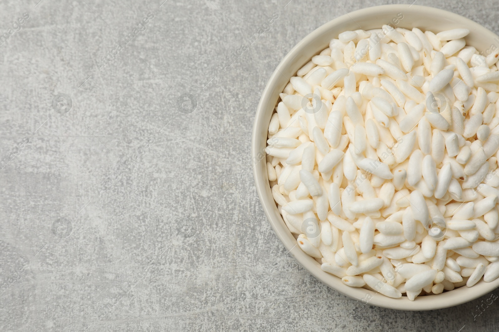 Photo of Puffed rice in bowl on light grey table, top view. Space for text