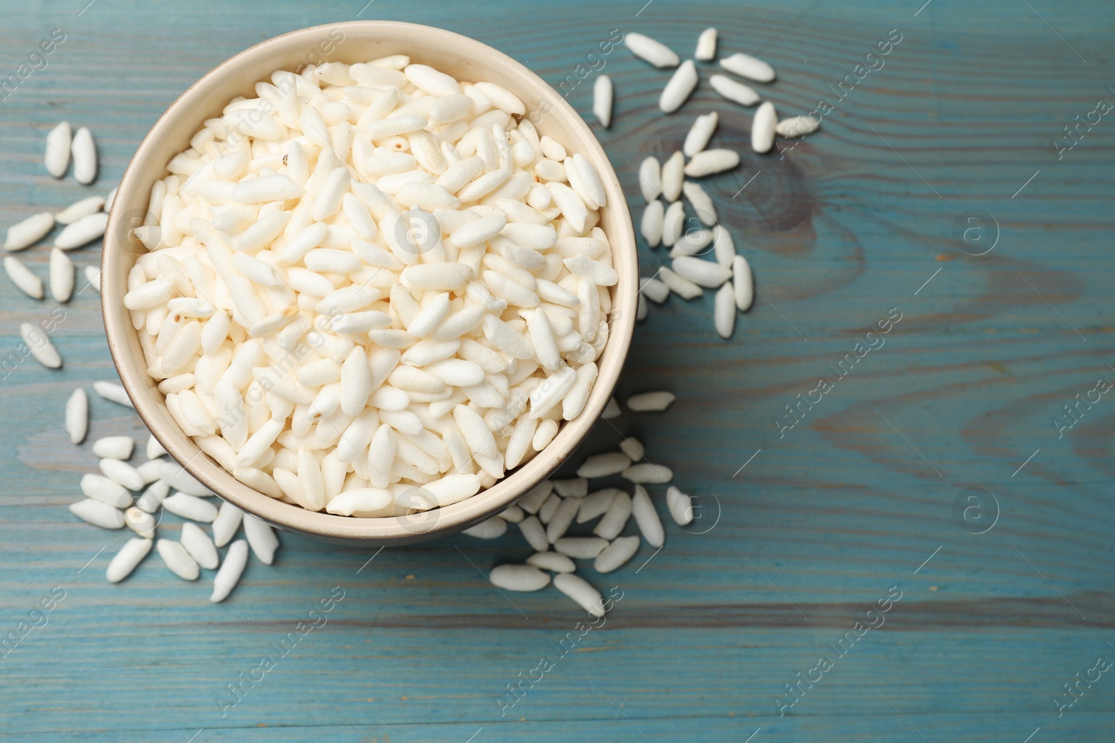 Photo of Puffed rice in bowl on light blue wooden table, top view. Space for text