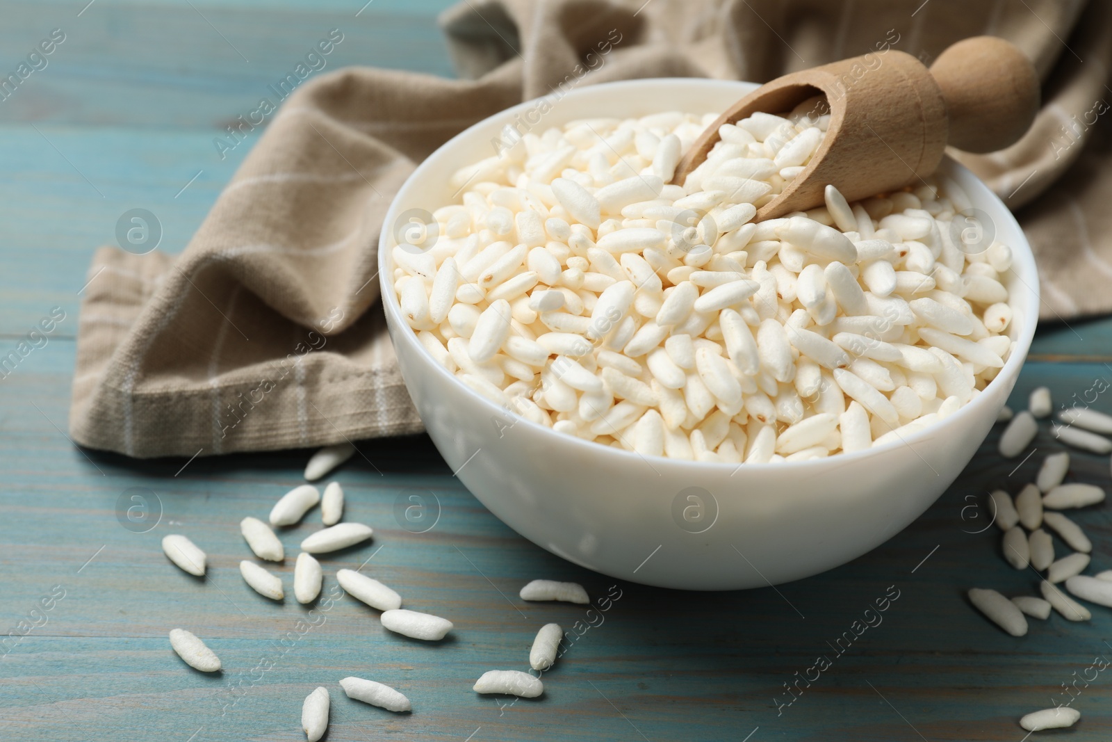 Photo of Puffed rice in bowl and scoop on light blue wooden table, closeup