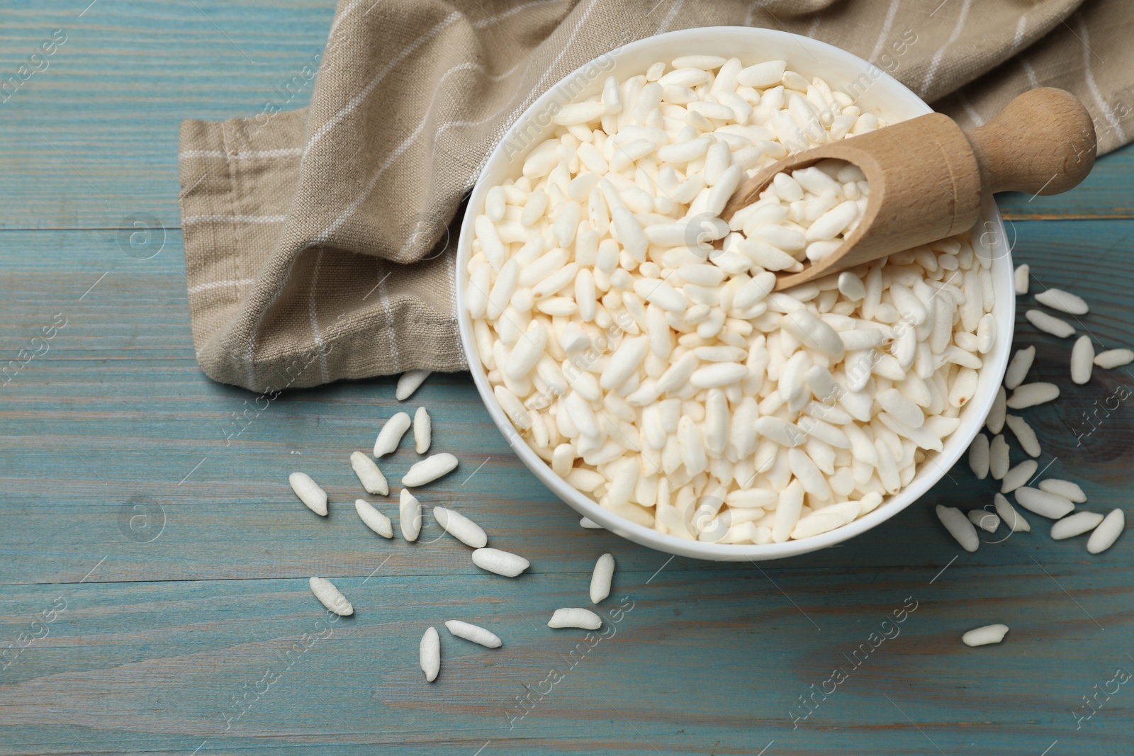 Photo of Puffed rice in bowl and scoop on light blue wooden table, flat lay