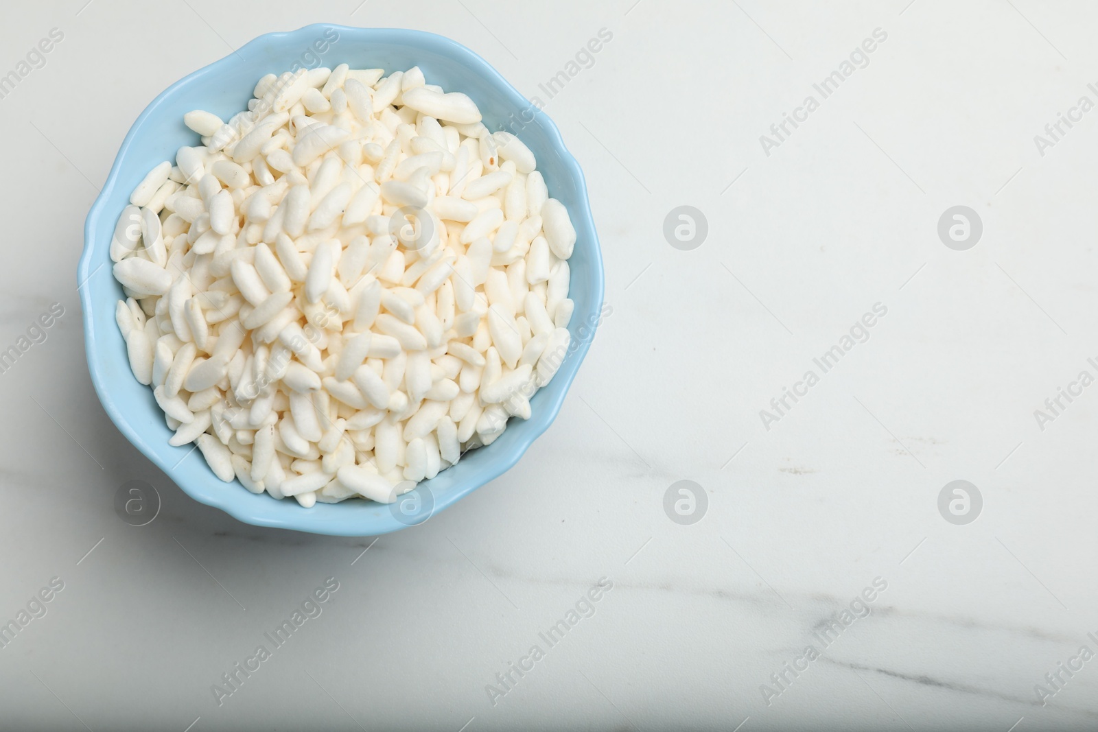 Photo of Puffed rice in bowl on white marble table, top view. Space for text