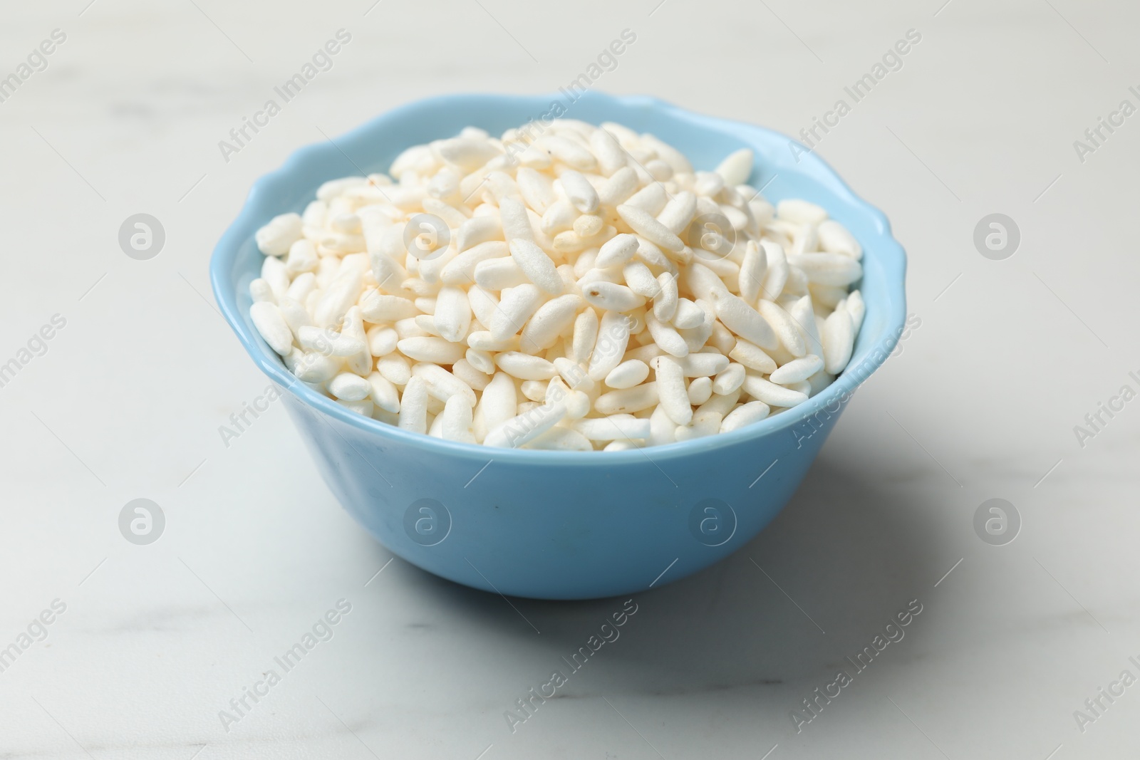 Photo of Puffed rice in bowl on white marble table, closeup