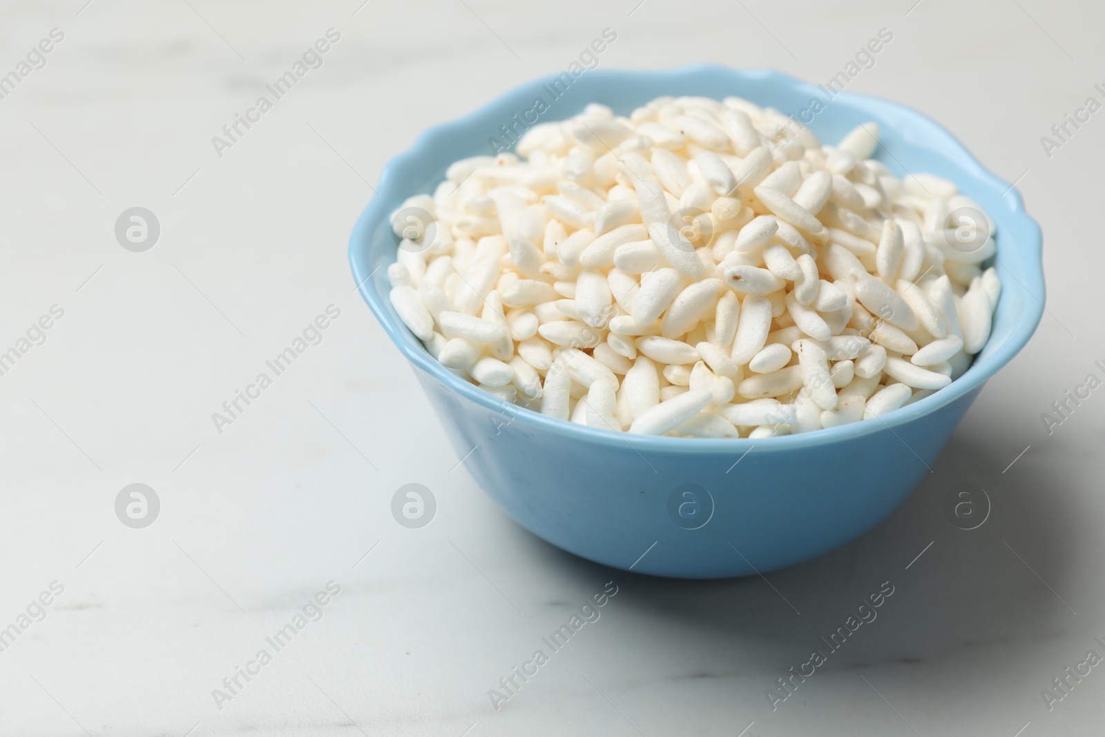 Photo of Puffed rice in bowl on white marble table, closeup. Space for text