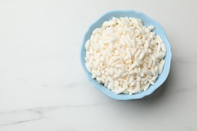 Photo of Puffed rice in bowl on white marble table, top view. Space for text