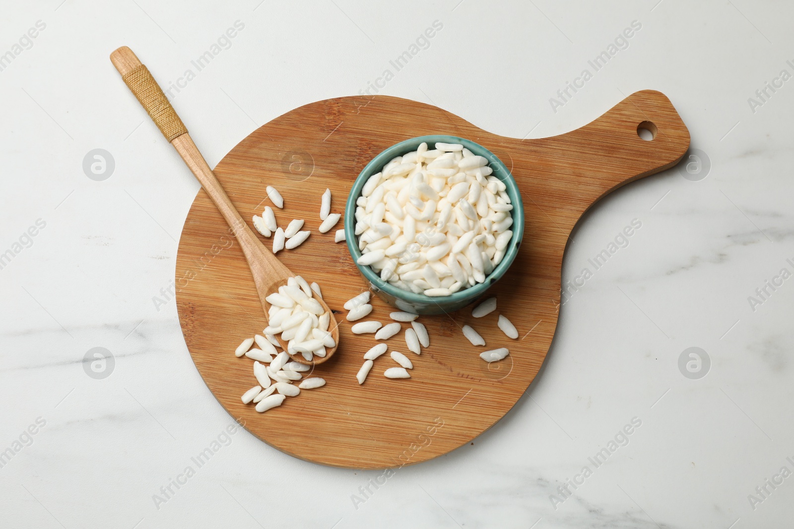 Photo of Puffed rice in bowl and spoon on white marble table, top view